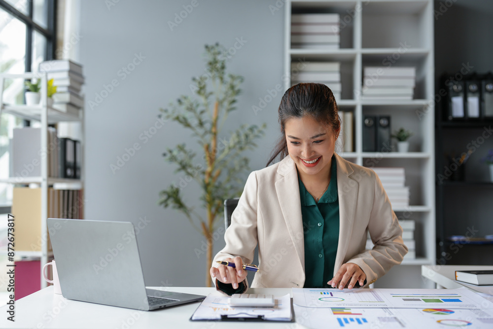 Asian business woman happily recording data on laptop Details from the graph Business income charts in real estate, taxes, management, technology marketing online in the office.