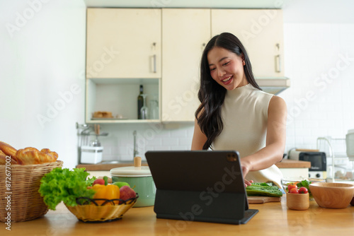Beautiful Asian woman practicing making vegetable salad Fruits are eaten in a relaxed way at home. View social media online on laptop healthy eating Weight loss and dieting healthy food concept.