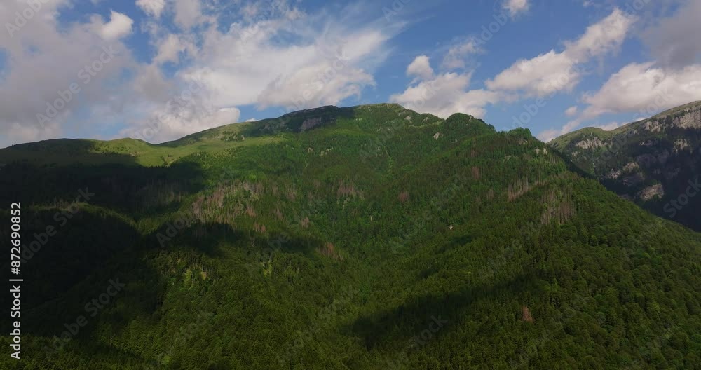 Tall mountain ranges covered in dense green forests, on a sunny day, cloudy sky, rising drone shot Tall mountain ranges covered in dense green forests, on a sunny day, cloudy sky, rising drone shot