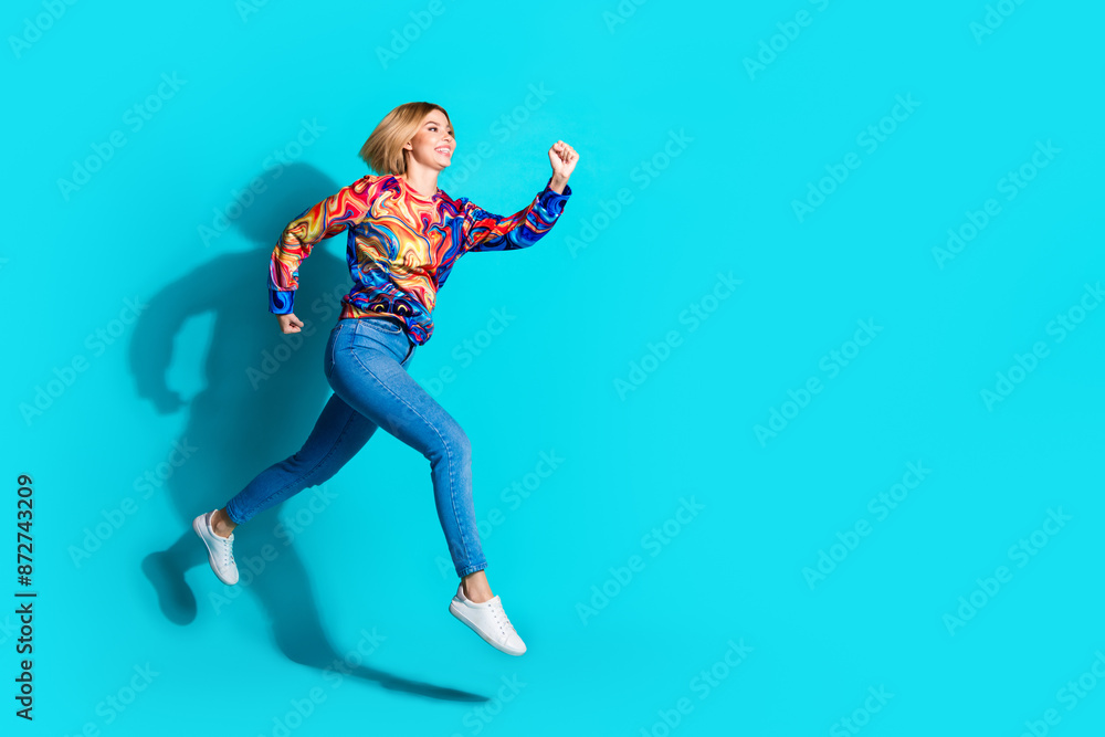 Full size photo of optimistic pretty girl dressed print shirt jeans look at sale run to empty space isolated on blue color background Full size photo of optimistic pretty girl dressed print shirt jeans look at sale run to empty space isolated on blue color background