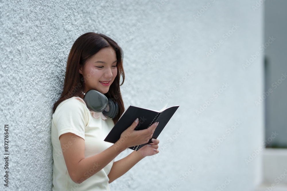 Attractive Asian female student standing holding a backpack and textbooks Smiling and looking at the camera while leaning against the background. learning concept new study online teenagers. Attractive Asian female student standing holding a backpack and textbooks Smiling and looking at the camera while leaning against the background. learning concept new study online teenagers.