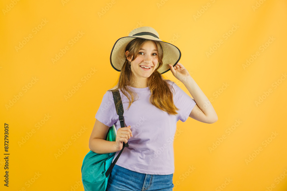 Happy little cute girl traveler carries a hiking backpack, travels on a hike, stands on a yellow background, wears a stylish hat, has a joyful expression on her face, loves to travel Happy little cute girl traveler carries a hiking backpack, travels on a hike, stands on a yellow background, wears a stylish hat, has a joyful expression on her face, loves to travel