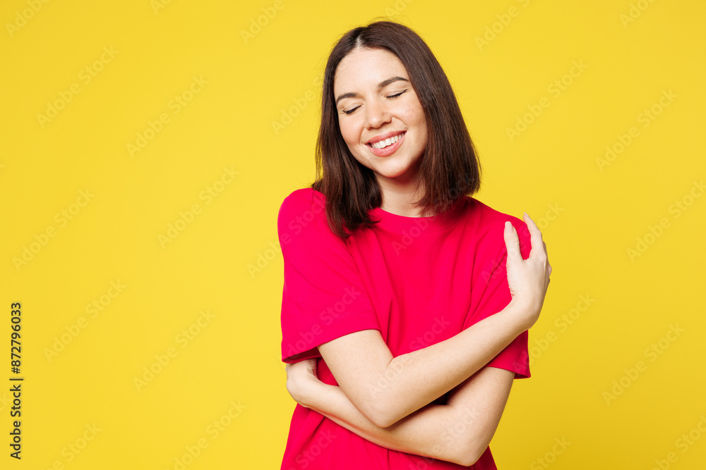 Young smiling happy cheerful fun cool woman she wearing pink t-shirt casual clothes hold hug embrace herself, close eyes isolated on plain yellow orange background studio portrait. Lifestyle concept. Young smiling happy cheerful fun cool woman she wearing pink t-shirt casual clothes hold hug embrace herself, close eyes isolated on plain yellow orange background studio portrait. Lifestyle concept.