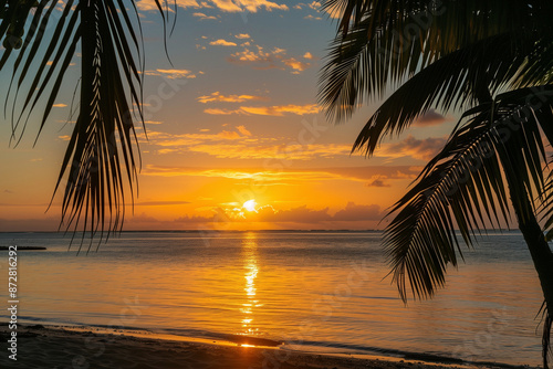 stunning view of a tropical beach at sunset, where the golden sun is dipping below the horizon, casting a warm glow over the tranquil waters. Palm trees frame the foreground, their