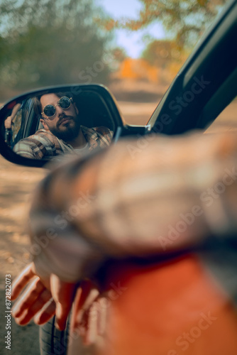 Fotografie A view of a car's rearview mirror reflecting a portrait of a man, a traveling enthusiast pausing to relax and enjoy the scenery