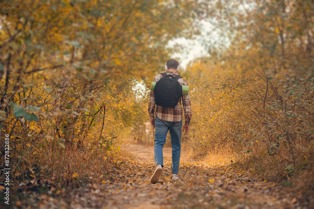Backpacker facing away, walking into the forest; a man power walking in the autumn woods. Backpacker facing away, walking into the forest; a man power walking in the autumn woods.