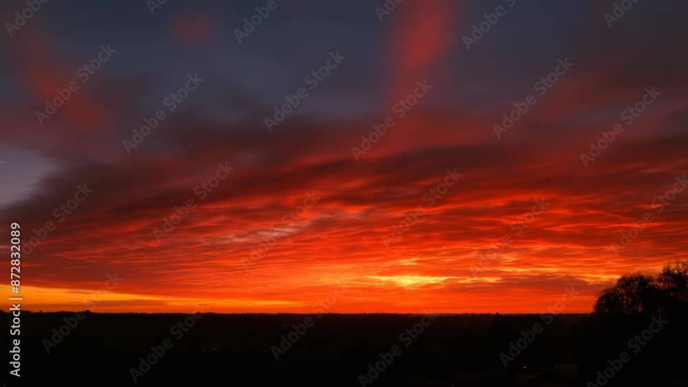 A vibrant sunset with fiery red and orange clouds spreading across the sky, silhouetting the dark landscape below, timelapse A vibrant sunset with fiery red and orange clouds spreading across the sky, silhouetting the dark landscape below, timelapse