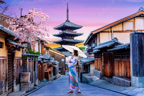 Fotografie Scenic cityscape of Yasaka pagoda in Kyoto with a young Japanese woman in a traditional Kimono dress during full bloom cherry blossom