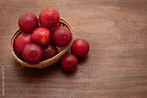 A wooden basket full of fresh Cherry Plum (Prunus cerasifera) fruits, on a wooden background. photo