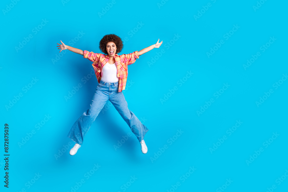 Full size photo of attractive young woman jump star pose dressed stylish checkered clothes isolated on blue color background Full size photo of attractive young woman jump star pose dressed stylish checkered clothes isolated on blue color background