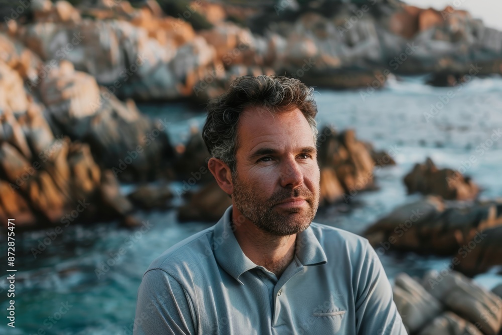 Portrait of a tender man in his 40s wearing a breathable golf polo in rocky shoreline background