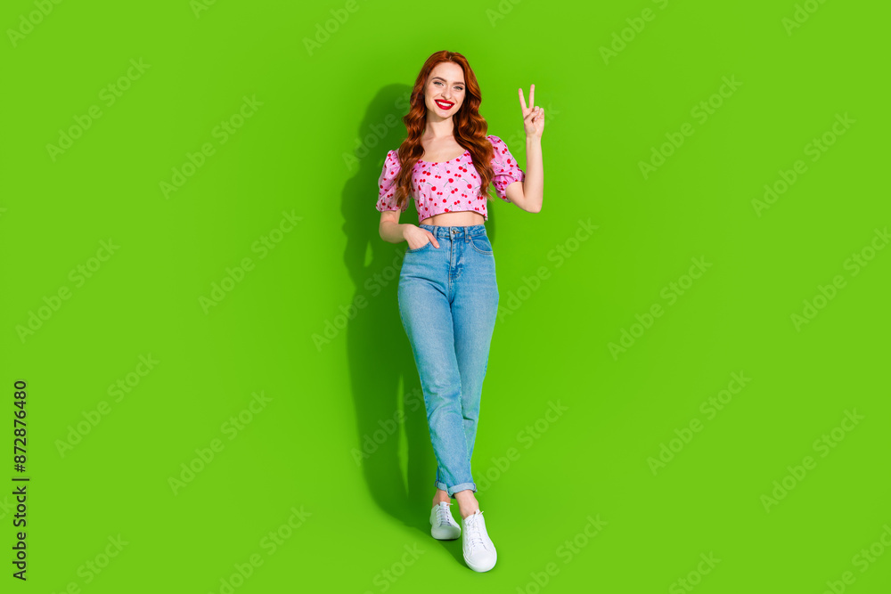 Full length photo of shiny attractive lady dressed print top showing v-sign empty space isolated green color background Full length photo of shiny attractive lady dressed print top showing v-sign empty space isolated green color background