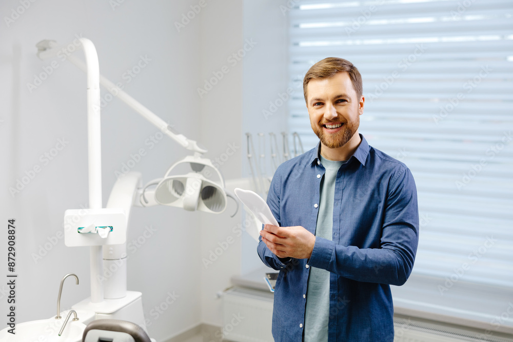 Obraz premium Handsome male patient looking at his beautiful smile standing at the dental office