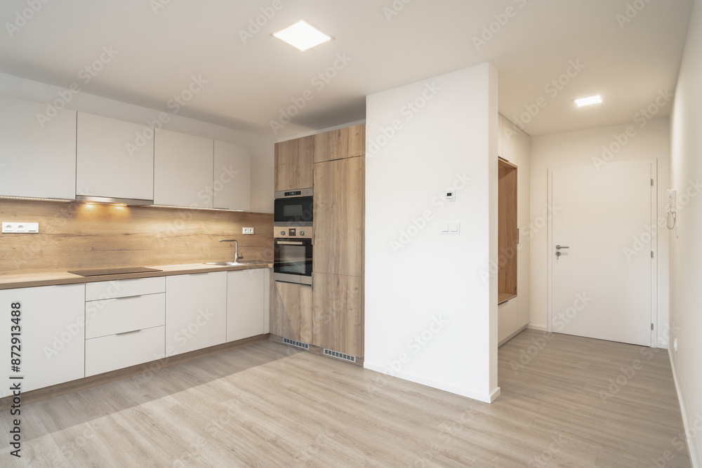 A modern kitchen with white cabinets, wooden countertops, built-in appliances, under-cabinet lighting, light wooden flooring, an entryway with a white door, and a wooden bench. A modern kitchen with white cabinets, wooden countertops, built-in appliances, under-cabinet lighting, light wooden flooring, an entryway with a white door, and a wooden bench.