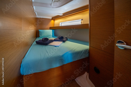 Sailing yacht interior. Double cabin on a charter yacht. Bareboat yacht interior - wood trim, light mattress and bedding, plenty of light from portholes. Comfortable berth for cruise on seas, oceans