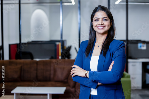 confident young indian businesswoman standing in corporate office smiling looking at camera. entrepreneur and workspace concept.