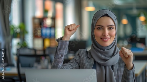 Exciting hijab businesswoman in front of the laptop, hand in the air, succesful target concept