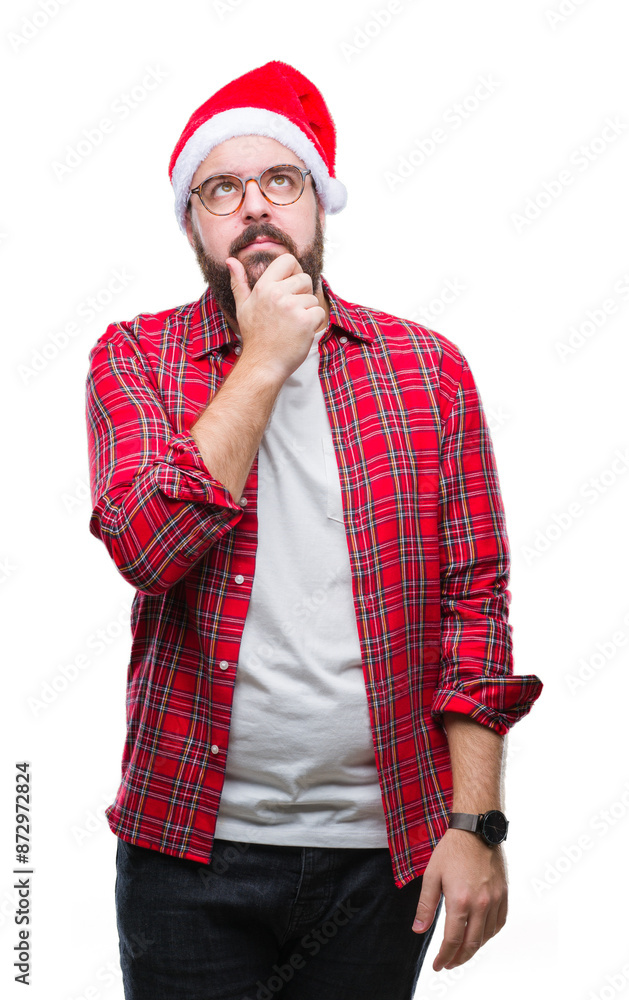 Young caucasian man wearing christmas hat over isolated background with hand on chin thinking about question, pensive expression. Smiling with thoughtful face. Doubt concept. Young caucasian man wearing christmas hat over isolated background with hand on chin thinking about question, pensive expression. Smiling with thoughtful face. Doubt concept.