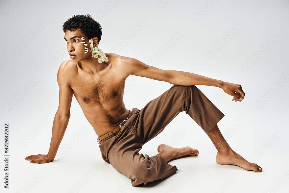 A young, muscular African American man poses with flowers on his body and face against a grey background. A young, muscular African American man poses with flowers on his body and face against a grey background.