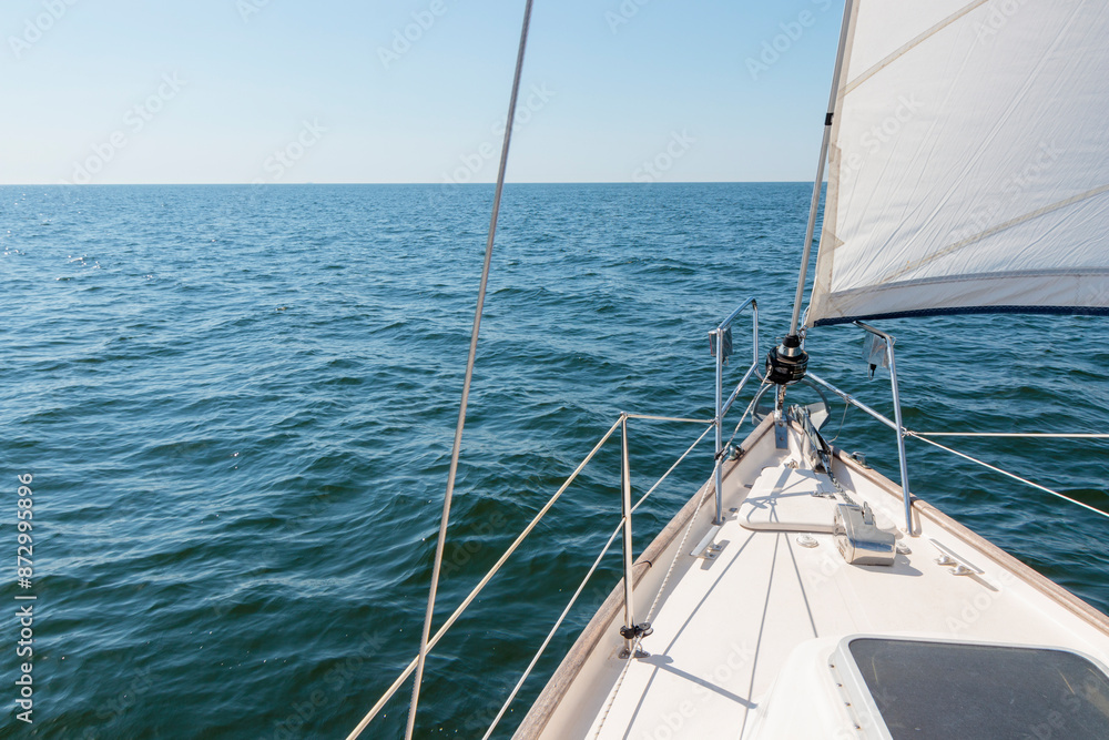 White yacht sailing on a sunny summer day. Top down view from the deck to the bow, mast and sails. Waves and water splashes. Clear blue sky. Gulf of Finland White yacht sailing on a sunny summer day. Top down view from the deck to the bow, mast and sails. Waves and water splashes. Clear blue sky. Gulf of Finland