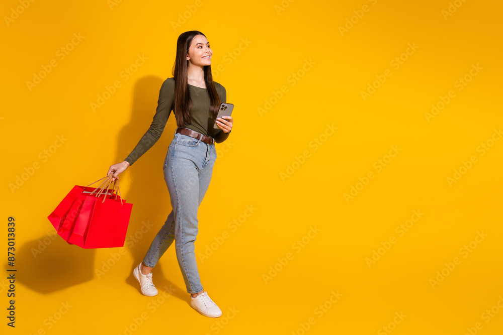 Fototapeta premium Full length photo of lovely teen lady go shopper device look empty space dressed stylish khaki garment isolated on yellow color background