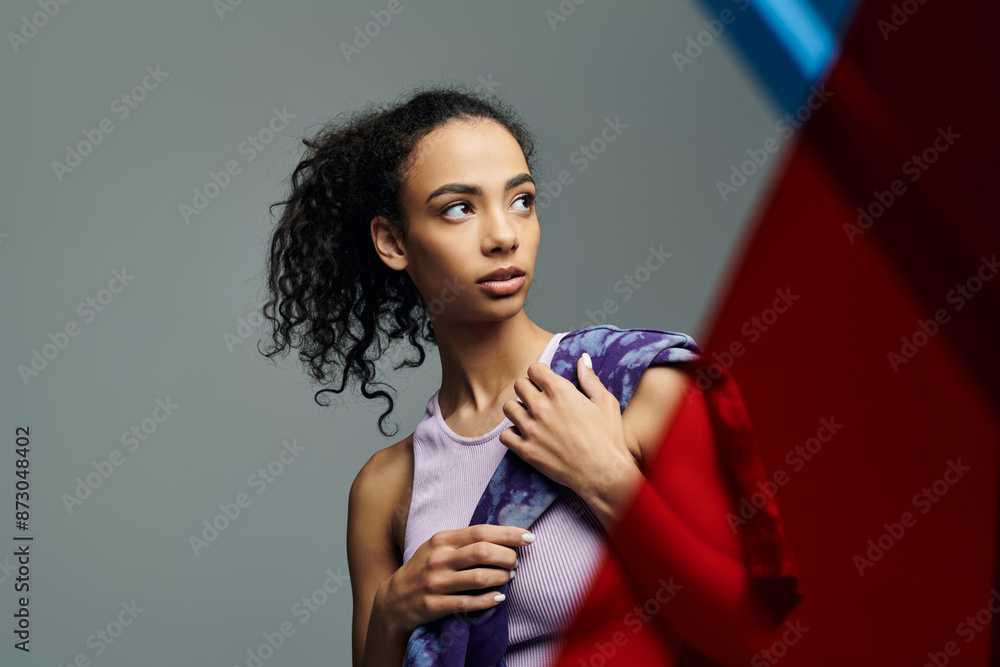 Naklejka premium A young woman with curly hair and a determined look holds a colorful scarf, showing off her athletic build.