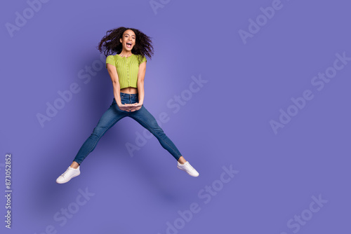Full length photo of lovely teen lady jump spread legs dressed stylish green garment isolated on purple color background