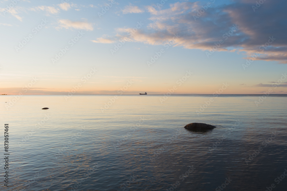 Fototapeta premium Seascape in the Baltic Sea during a calm summer evening after sunset, a cargo ship stands on the horizon.