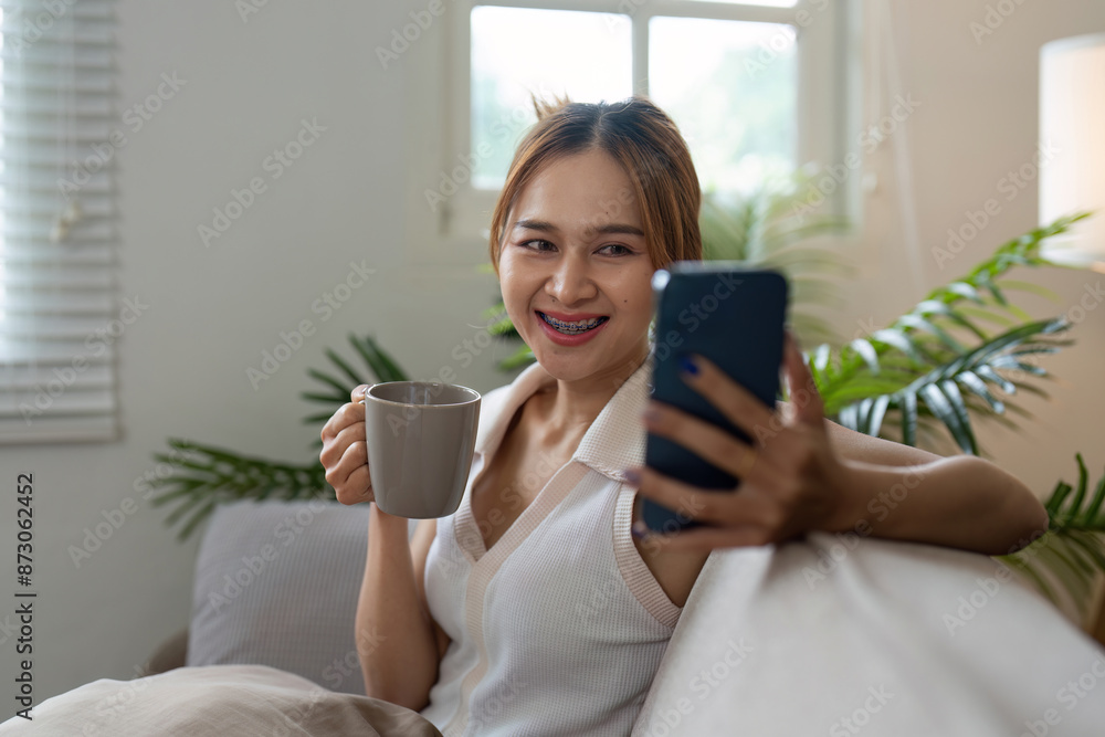 Young Woman Relaxing on Sofa with Coffee and Smartphone in Cozy Living Room Young Woman Relaxing on Sofa with Coffee and Smartphone in Cozy Living Room