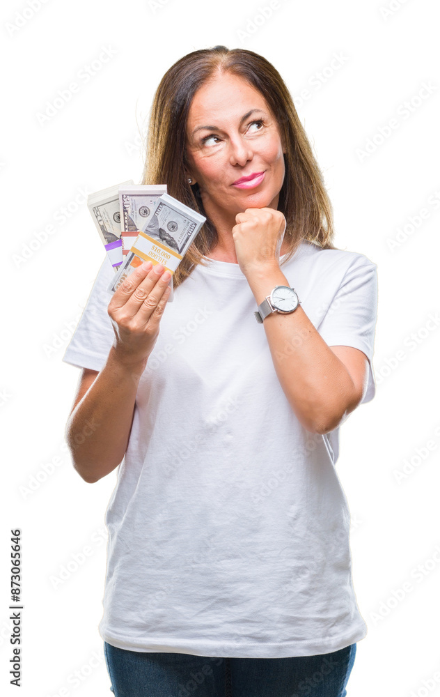 Middle age hispanic woman holding bunch of dollars over isolated background serious face thinking about question, very confused idea Middle age hispanic woman holding bunch of dollars over isolated background serious face thinking about question, very confused idea