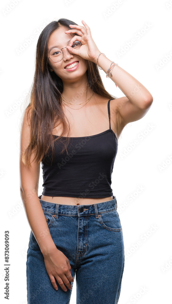 Young asian woman wearing glasses over isolated background doing ok gesture with hand smiling, eye looking through fingers with happy face. Young asian woman wearing glasses over isolated background doing ok gesture with hand smiling, eye looking through fingers with happy face.