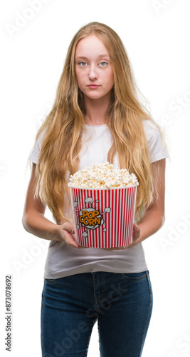 Blonde teenager woman eating pop corn with a confident expression on smart face thinking serious