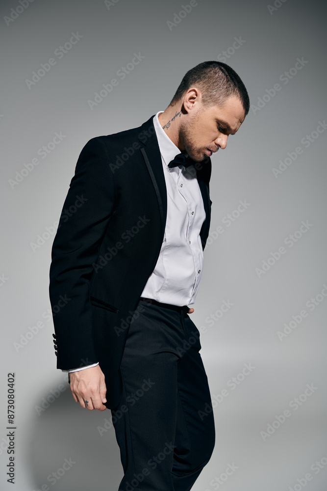 Man in tuxedo against grey backdrop, exuding quiet confidence. Man in tuxedo against grey backdrop, exuding quiet confidence.