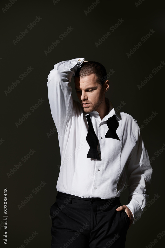A man in a white shirt and black bow tie poses with his hand on his head. A man in a white shirt and black bow tie poses with his hand on his head.