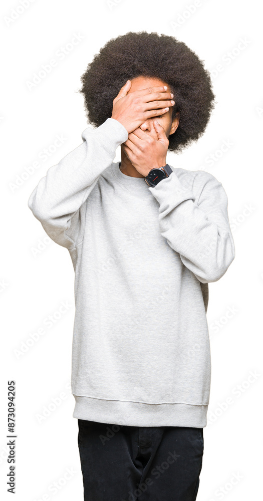 Young african american man with afro hair wearing sporty sweatshirt Covering eyes and mouth with hands, surprised and shocked. Hiding emotion Young african american man with afro hair wearing sporty sweatshirt Covering eyes and mouth with hands, surprised and shocked. Hiding emotion