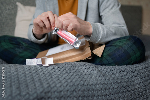 Midsection of man tearing packet of vape pen while sitting on bed