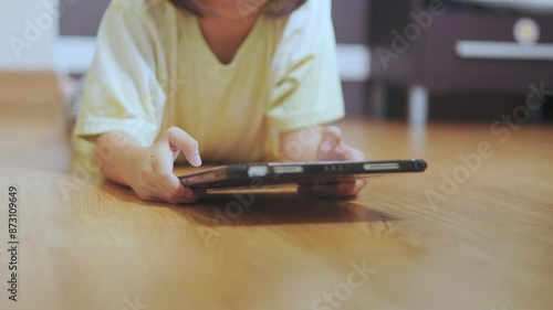Selective focus and closed up hands of child lies on the floor, playing or using tablet, in a cozy room highlighting the positive impact of the digital device for e-learning and remote education.
