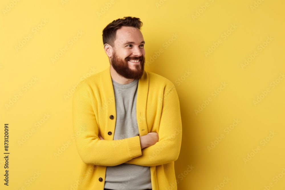 Portrait of a grinning man in his 30s wearing a chic cardigan while standing against pastel yellow background Portrait of a grinning man in his 30s wearing a chic cardigan while standing against pastel yellow background