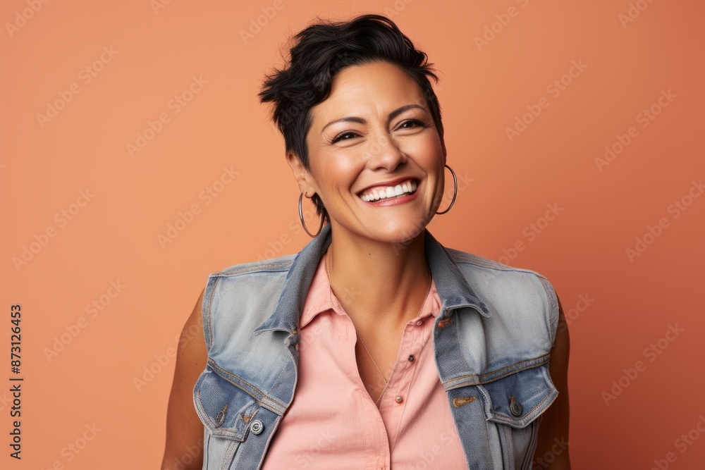 Portrait of a cheerful woman in her 40s wearing a rugged jean vest over pastel orange background Portrait of a cheerful woman in her 40s wearing a rugged jean vest over pastel orange background