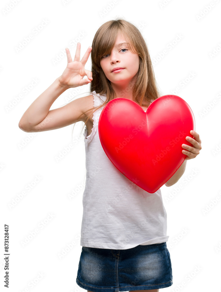 Young blonde toddler holding a red heart doing ok sign with fingers, excellent symbol Young blonde toddler holding a red heart doing ok sign with fingers, excellent symbol