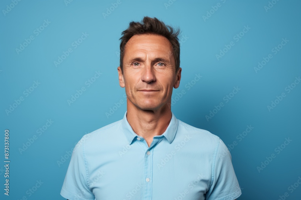 Portrait of a satisfied man in his 40s wearing a sporty polo shirt while standing against soft blue background Portrait of a satisfied man in his 40s wearing a sporty polo shirt while standing against soft blue background