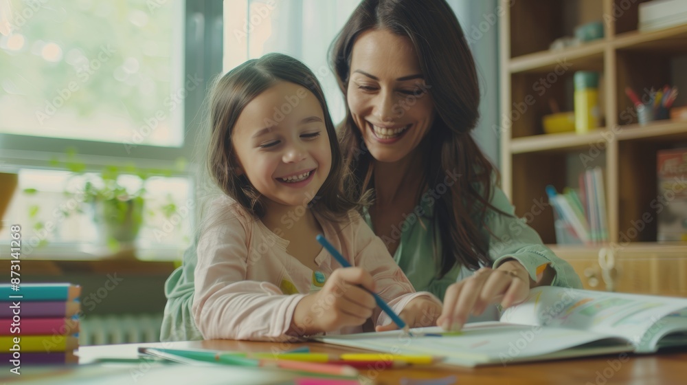 Her mother helps this adorable Caucasian girl do her schoolwork at the table. Happy young woman educating her daughter at home. A homeschooling mother Her mother helps this adorable Caucasian girl do her schoolwork at the table. Happy young woman educating her daughter at home. A homeschooling mother