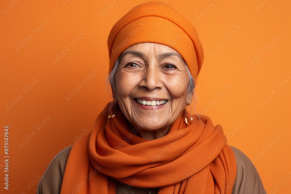 Portrait of a smiling indian woman in her 60s donning a warm wool beanie on soft orange background Portrait of a smiling indian woman in her 60s donning a warm wool beanie on soft orange background