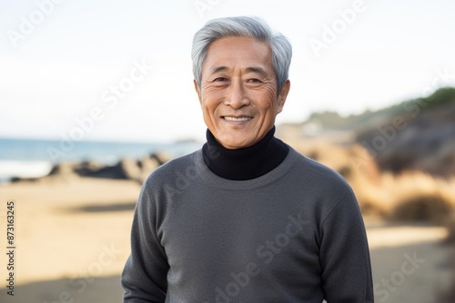 Portrait of a content asian man in his 80s wearing a classic turtleneck sweater isolated in sandy beach background