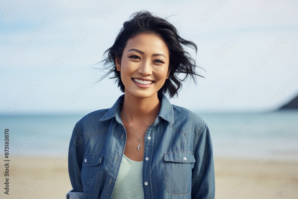 Portrait of a grinning asian woman in her 20s sporting a versatile denim shirt in sandy beach background Portrait of a grinning asian woman in her 20s sporting a versatile denim shirt in sandy beach background