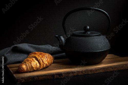 Foto teapot and a croissant on a wooden board