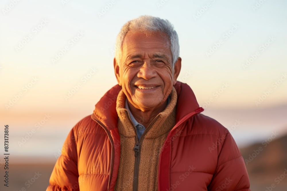 Portrait of a satisfied indian man in his 70s sporting a quilted insulated jacket in front of stunning sunset beach background Portrait of a satisfied indian man in his 70s sporting a quilted insulated jacket in front of stunning sunset beach background