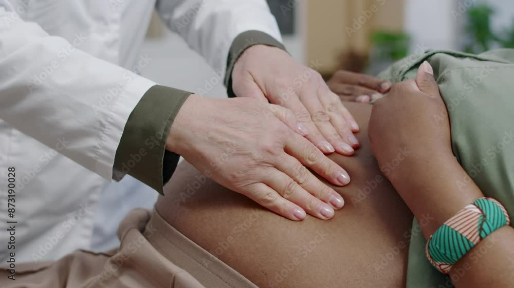Close-up of hands of unrecognizable gynecologist carefully checking unborn baby position by touching abdomen of pregnant African American woman Close-up of hands of unrecognizable gynecologist carefully checking unborn baby position by touching abdomen of pregnant African American woman