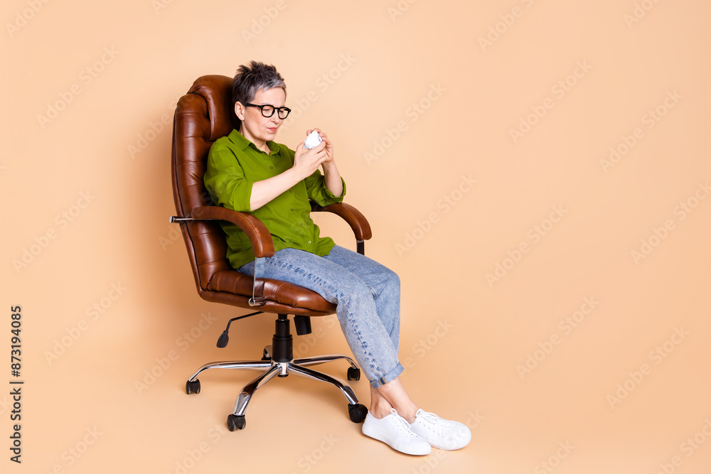Full body photo of attractive retired woman sit armchair stress crumpled paper dressed green clothes isolated on beige color background Full body photo of attractive retired woman sit armchair stress crumpled paper dressed green clothes isolated on beige color background