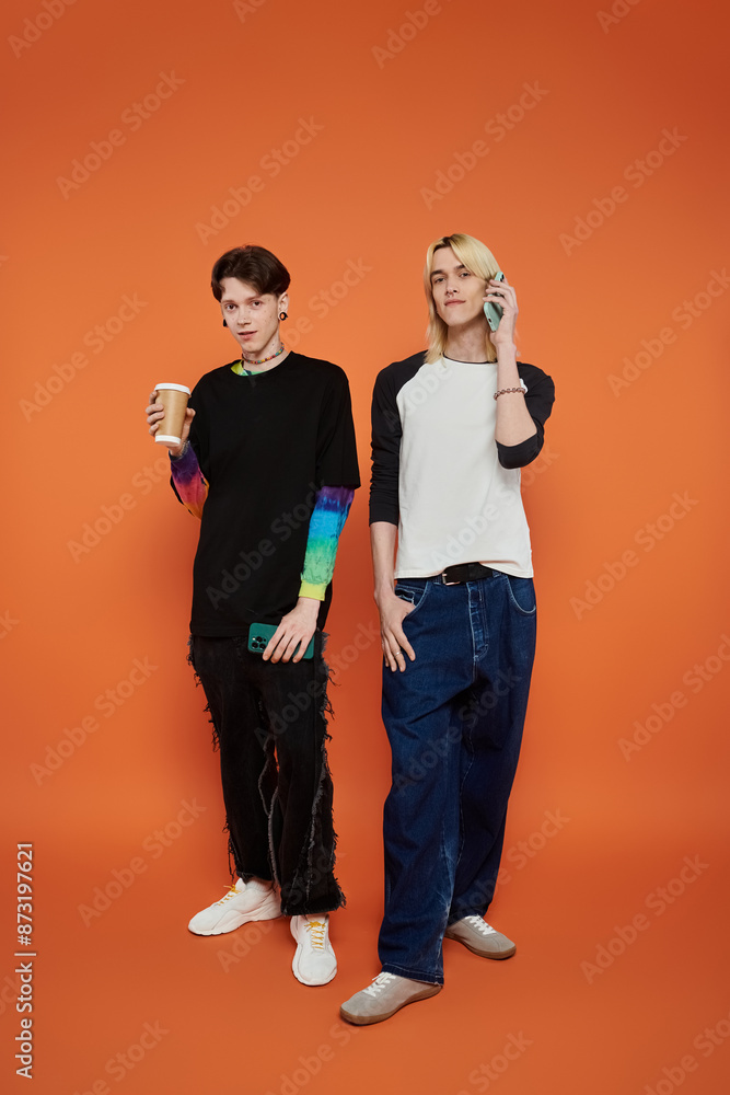 Two young friends wearing colorful outfits pose against an orange background. Two young friends wearing colorful outfits pose against an orange background.